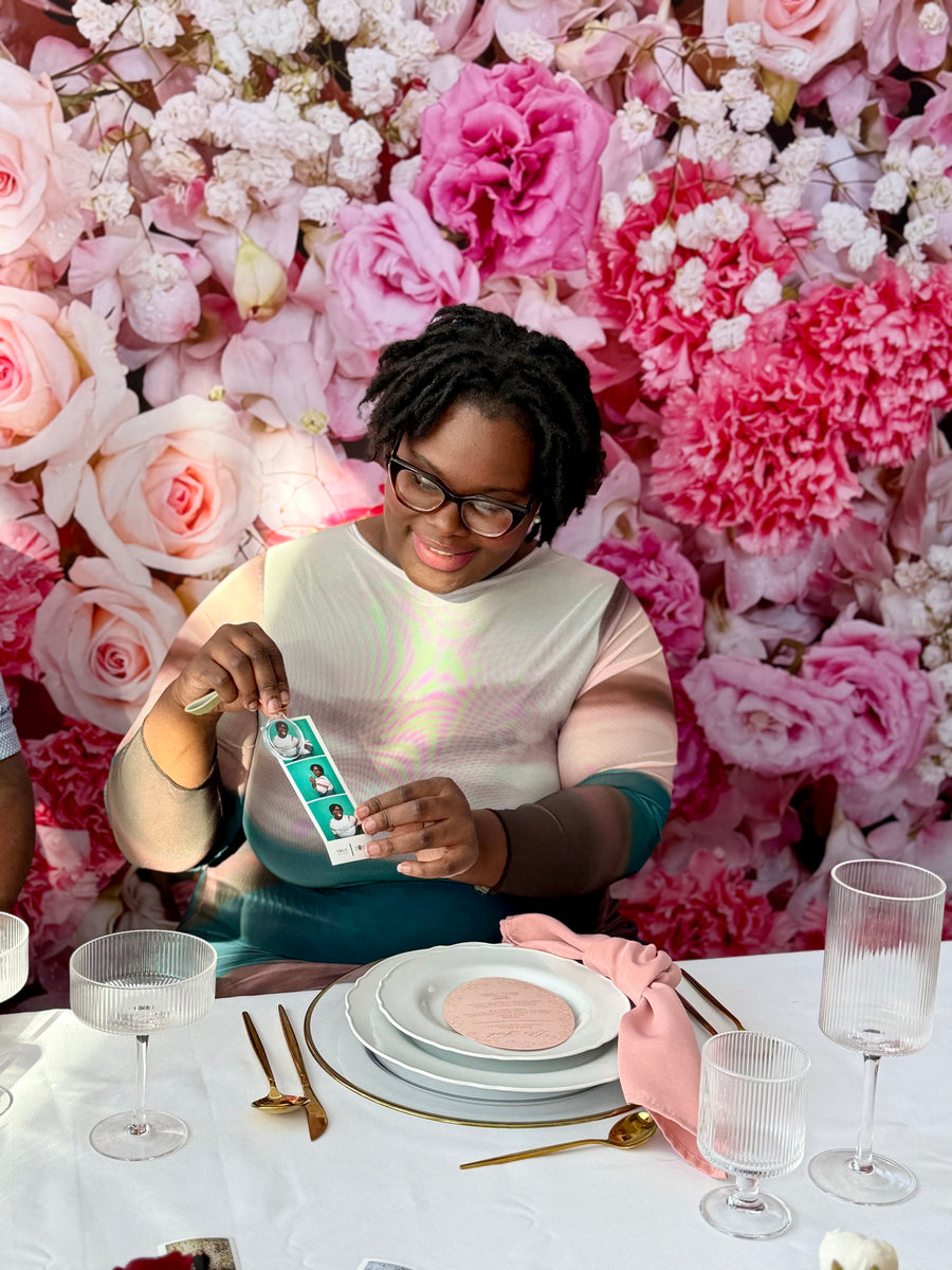 Guest with photo strips in front of a printed pink floral backdrop